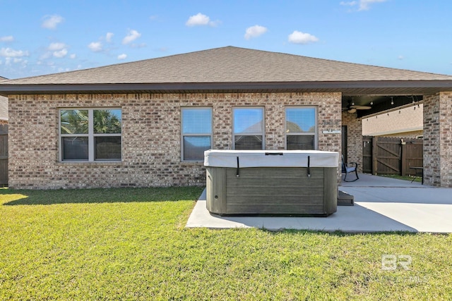 back of house featuring a hot tub, a lawn, a patio, fence, and brick siding