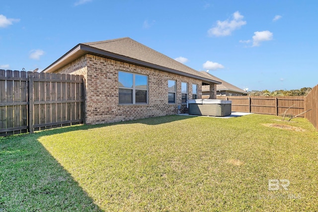 rear view of house featuring a fenced backyard, brick siding, roof with shingles, a lawn, and a hot tub