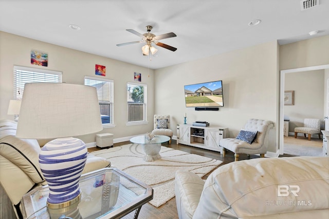 living room featuring a ceiling fan, wood finished floors, visible vents, and baseboards