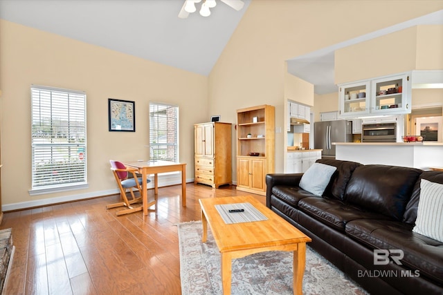 living room with light wood-type flooring, baseboards, high vaulted ceiling, and a wealth of natural light