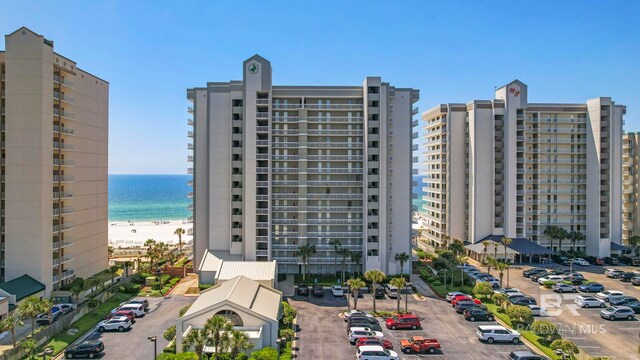 view of building exterior featuring uncovered parking, a water view, and a beach view
