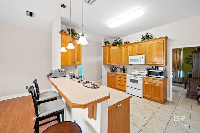 kitchen featuring a kitchen bar, kitchen peninsula, white appliances, light hardwood / wood-style flooring, and hanging light fixtures