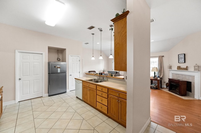 kitchen with white dishwasher, sink, hanging light fixtures, stainless steel fridge, and light hardwood / wood-style floors