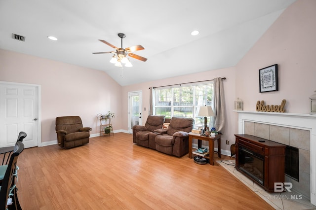 living room featuring ceiling fan, a fireplace, vaulted ceiling, and light wood-type flooring