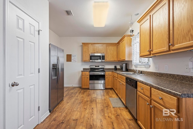 kitchen with appliances with stainless steel finishes, sink, and light hardwood / wood-style floors