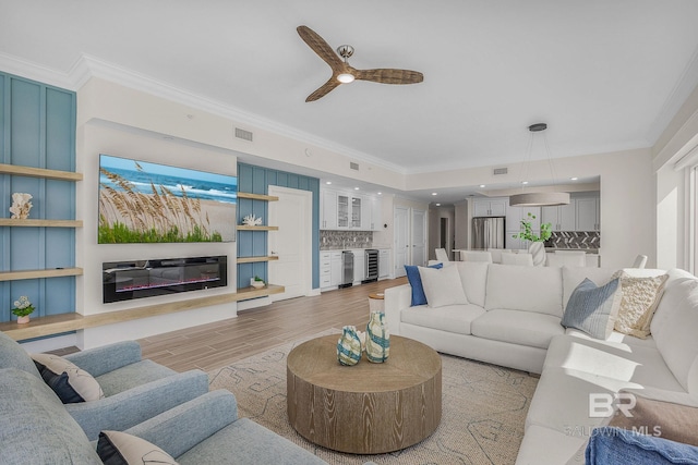 living room with light wood-style flooring, visible vents, ornamental molding, a dry bar, and beverage cooler