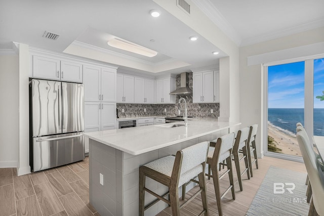 kitchen featuring a kitchen breakfast bar, wall chimney range hood, visible vents, freestanding refrigerator, and a peninsula