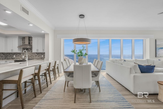 dining space with light wood-type flooring, ornamental molding, a water view, and visible vents