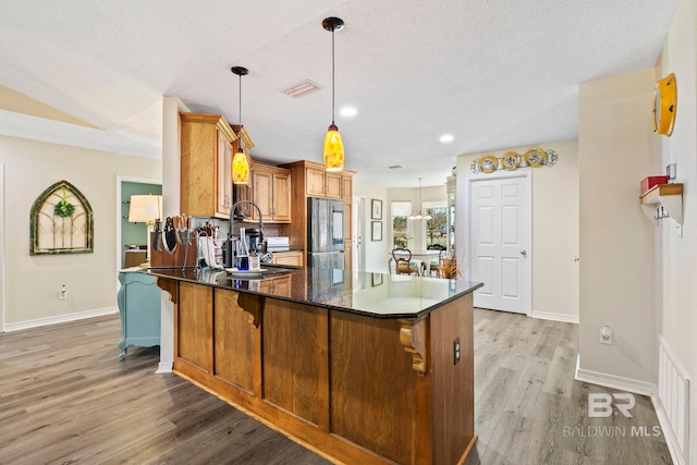 kitchen featuring kitchen peninsula, stainless steel fridge, dark stone counters, light hardwood / wood-style flooring, and hanging light fixtures