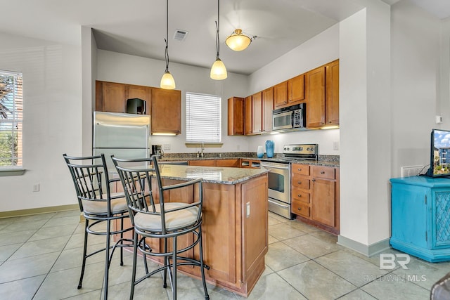 kitchen with a breakfast bar, visible vents, appliances with stainless steel finishes, brown cabinets, and dark stone counters