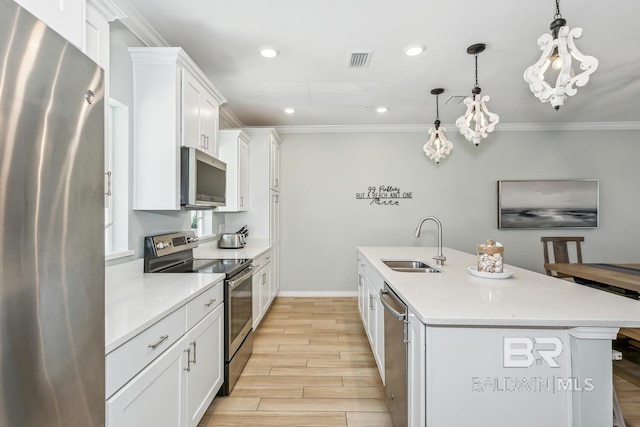 kitchen with pendant lighting, sink, appliances with stainless steel finishes, white cabinets, and a center island with sink