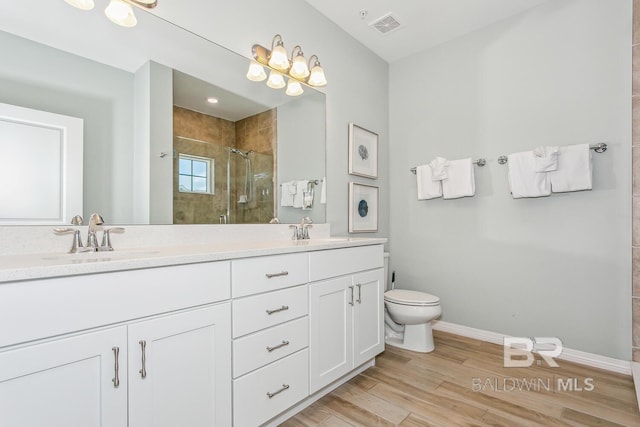 bathroom featuring a tile shower, hardwood / wood-style flooring, toilet, and double sink vanity