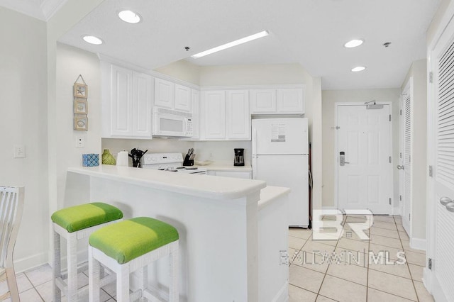 kitchen with a kitchen bar, light tile patterned floors, light countertops, white cabinets, and white appliances
