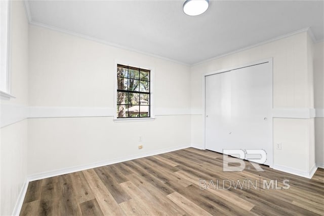 unfurnished bedroom with a closet, hardwood / wood-style floors, a baseboard heating unit, and ornamental molding