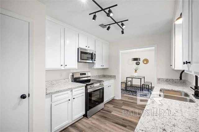 kitchen featuring track lighting, white cabinets, sink, light stone countertops, and appliances with stainless steel finishes