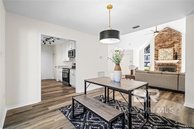 dining room with dark hardwood / wood-style flooring, lofted ceiling, and a brick fireplace