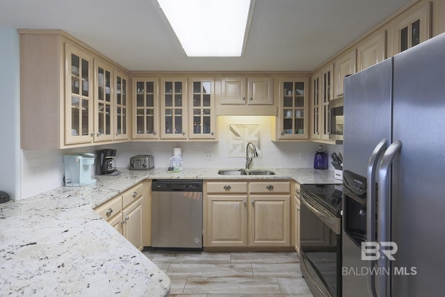 kitchen featuring light stone counters, a sink, tasteful backsplash, light brown cabinets, and stainless steel appliances