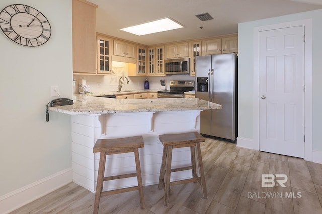 kitchen with a peninsula, appliances with stainless steel finishes, light wood-style floors, and light brown cabinetry