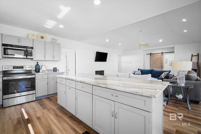 kitchen featuring gray cabinetry, ceiling fan, a barn door, appliances with stainless steel finishes, and hardwood / wood-style flooring