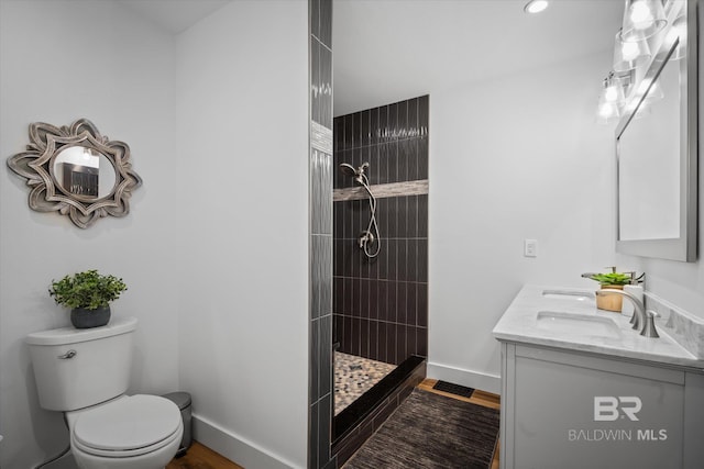 bathroom with hardwood / wood-style flooring, vanity, toilet, and tiled shower