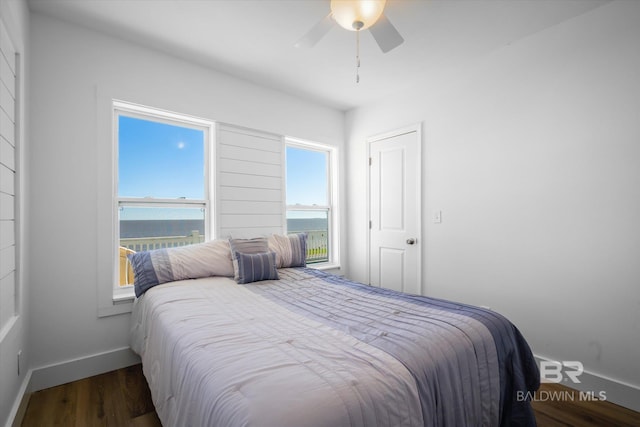 bedroom with ceiling fan, a water view, and dark wood-type flooring