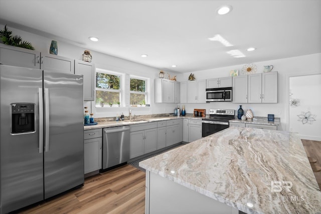 kitchen with hardwood / wood-style floors, sink, gray cabinets, appliances with stainless steel finishes, and light stone counters