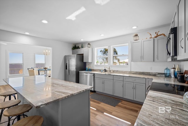 kitchen with appliances with stainless steel finishes, a center island, light hardwood / wood-style floors, and light stone counters