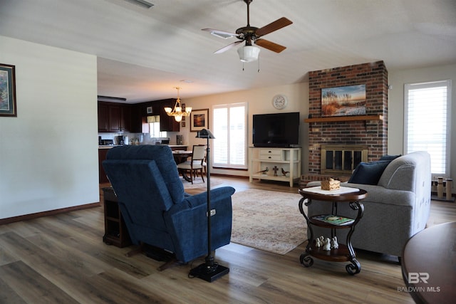 living room with ceiling fan with notable chandelier, hardwood / wood-style floors, and a fireplace