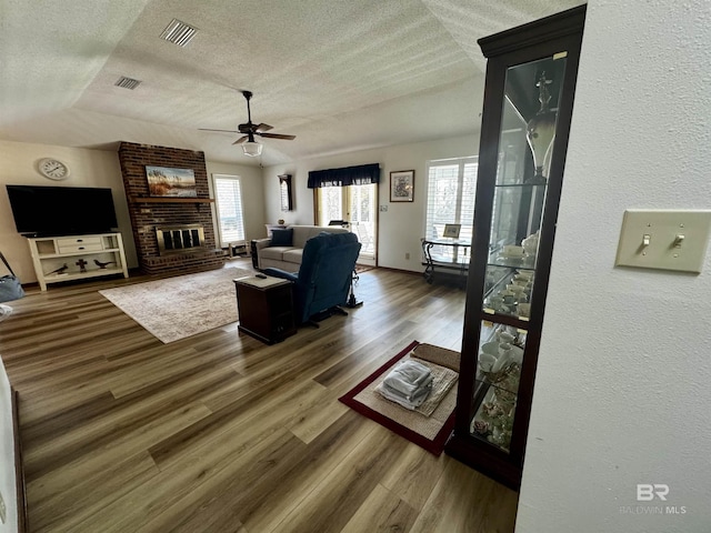 living room with wood-type flooring, ceiling fan, a textured ceiling, and a fireplace