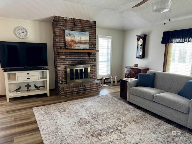 living room featuring wood-type flooring, ceiling fan, a textured ceiling, and a fireplace