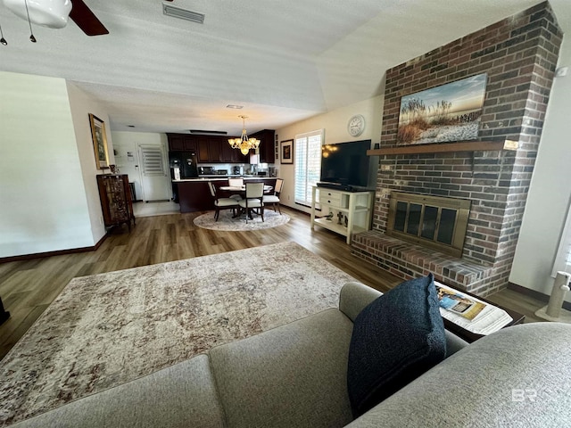 living room with ceiling fan with notable chandelier, a fireplace, dark hardwood / wood-style floors, and a textured ceiling