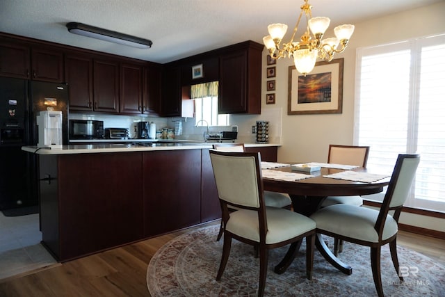 kitchen with dark brown cabinetry, decorative light fixtures, a notable chandelier, hardwood / wood-style floors, and black appliances