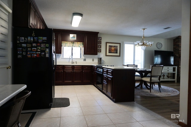 kitchen featuring sink, black fridge, decorative light fixtures, light tile patterned floors, and kitchen peninsula