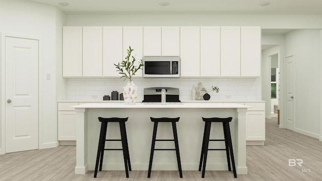 kitchen featuring a kitchen island with sink, range, stainless steel microwave, and white cabinets