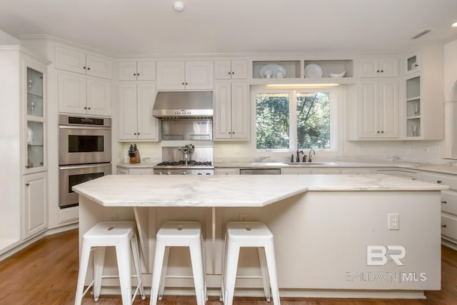 kitchen featuring white cabinets, a center island, extractor fan, and light stone counters