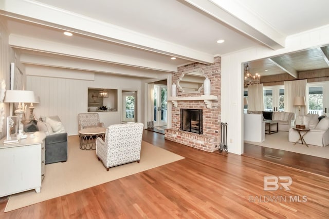 living room featuring beam ceiling, a chandelier, a fireplace, and hardwood / wood-style floors