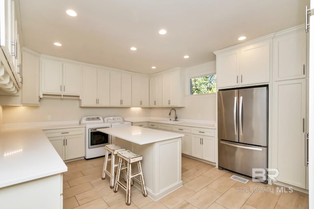 kitchen with washing machine and clothes dryer, a kitchen island, stainless steel fridge, a kitchen bar, and white cabinets