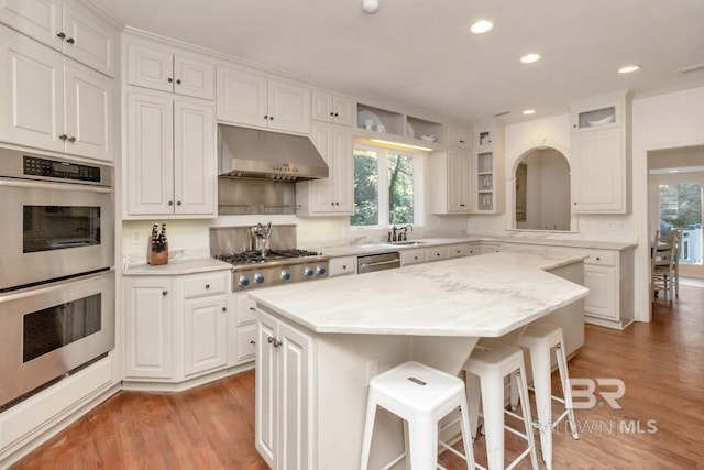 kitchen with appliances with stainless steel finishes, ventilation hood, white cabinets, a center island, and a breakfast bar area