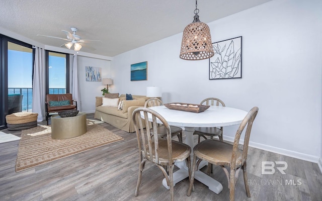 dining area featuring floor to ceiling windows, ceiling fan, a textured ceiling, wood finished floors, and baseboards