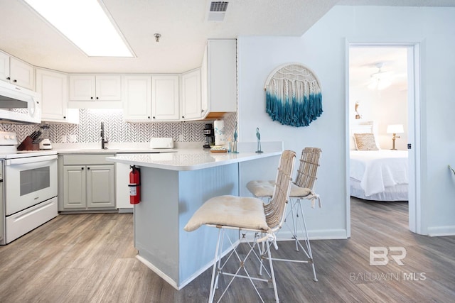 kitchen with a peninsula, white appliances, visible vents, light countertops, and tasteful backsplash