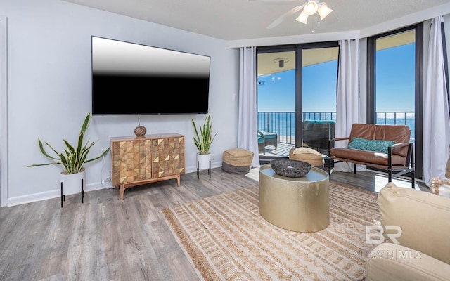 living area with a ceiling fan, expansive windows, baseboards, and wood finished floors