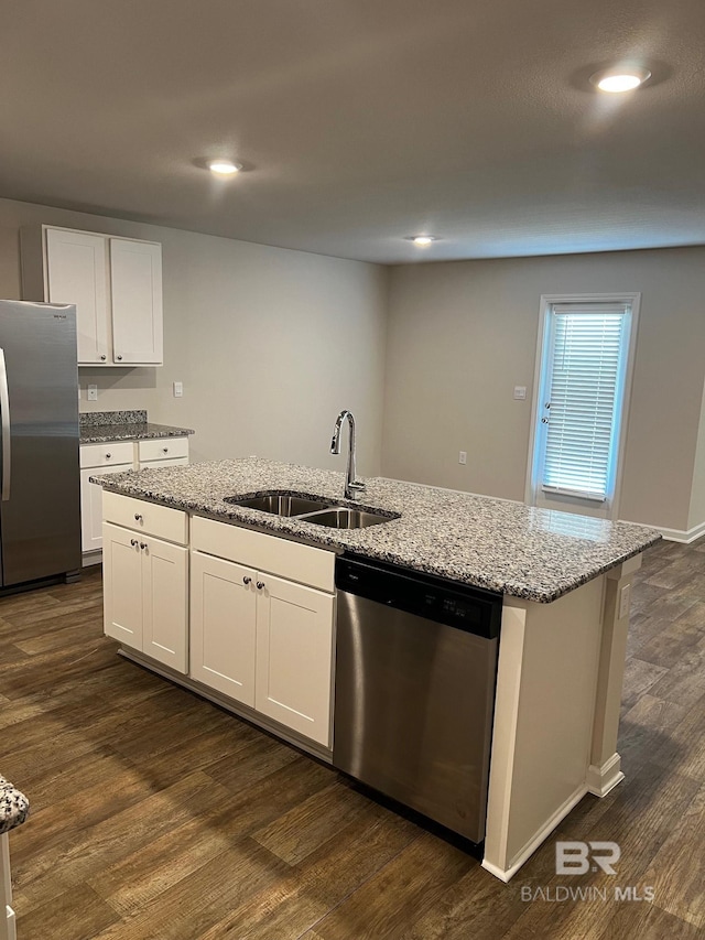 kitchen featuring dark wood-type flooring, a center island with sink, a sink, appliances with stainless steel finishes, and light stone countertops