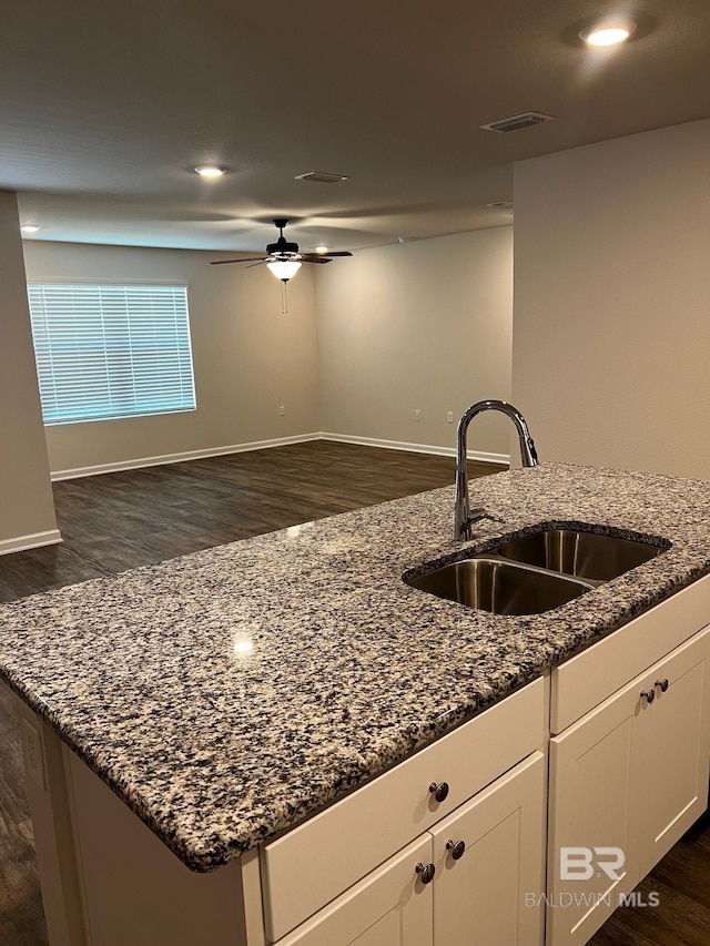 kitchen with dark wood finished floors, white cabinets, dark stone counters, and a sink