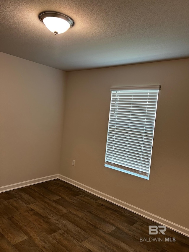 empty room featuring baseboards, a textured ceiling, and dark wood-style floors