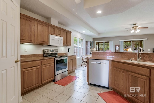 kitchen featuring stainless steel appliances, a raised ceiling, ceiling fan, sink, and light tile patterned floors