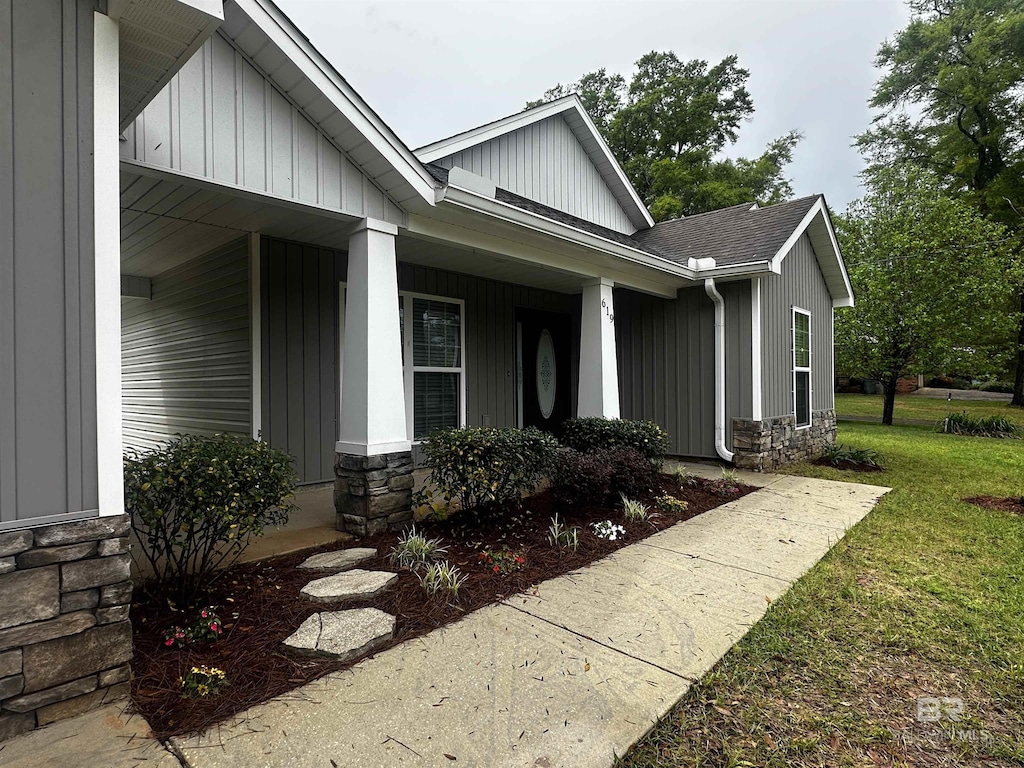property entrance featuring a shingled roof, covered porch, stone siding, and a lawn