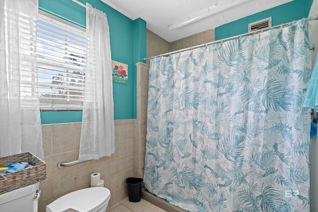 bathroom with tile walls, a textured ceiling, a shower with shower curtain, toilet, and tile patterned floors