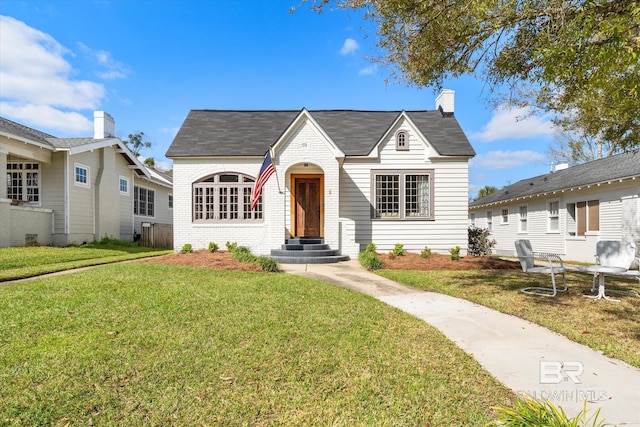 bungalow featuring brick siding, entry steps, a chimney, and a front yard