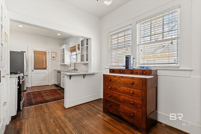 kitchen with a sink, dark wood finished floors, light countertops, glass insert cabinets, and dishwasher