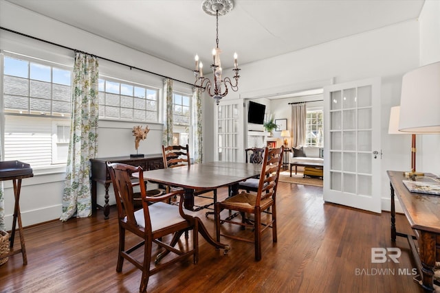 dining space featuring a fireplace, a notable chandelier, wood finished floors, and baseboards